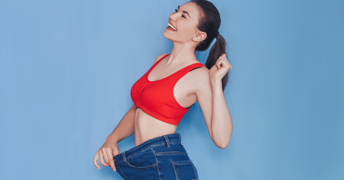 lovely woman holding the waist of her tight jeans while wearing a red shirt