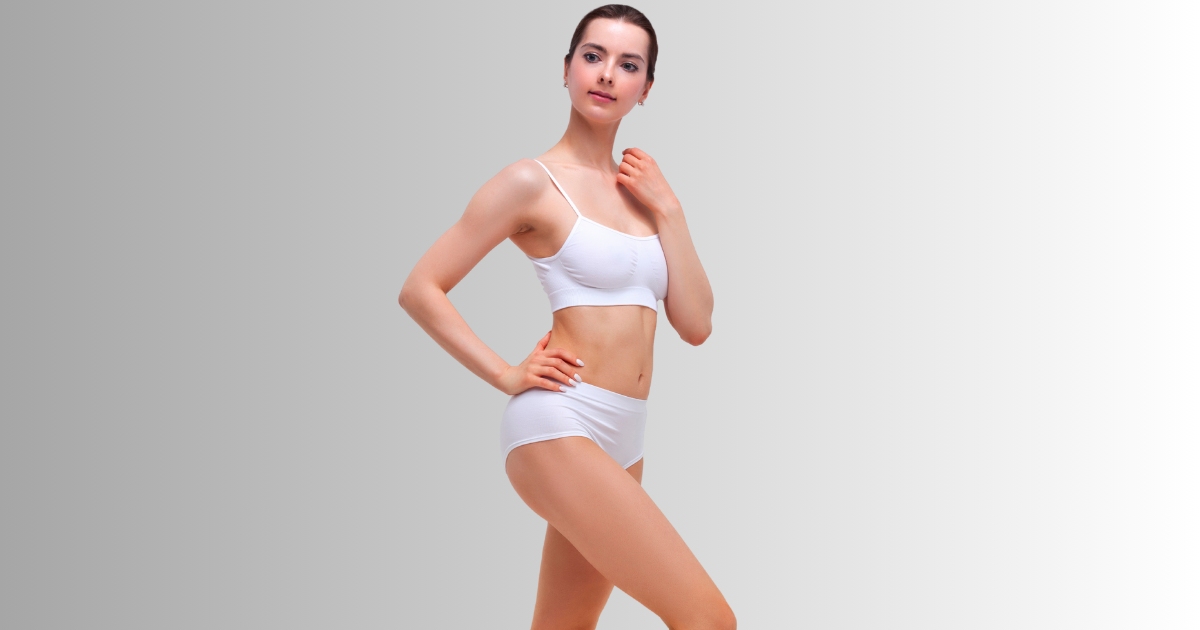 A woman wearing a white sports bra and white underwear stands in a confident pose against a light gray gradient background, with one hand on her hip and the other touching her neck.